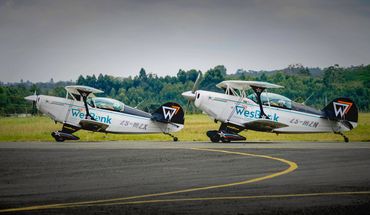 Two vintage biplanes parked on a runway with lush greenery in the background.
