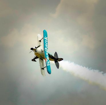 A stunt biplane performing a smoke trail maneuver in the sky.