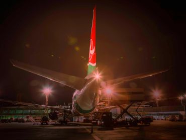 A Kenya Airways airplane on the tarmac at night with bright lights.