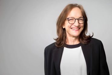 Smiling middle-aged woman with glasses in a casual black and white outfit.