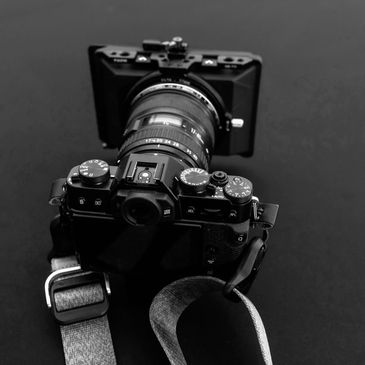Black and white photo of a vintage camera with a strap on a dark surface.