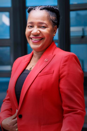 Smiling woman in a red blazer standing indoors.
