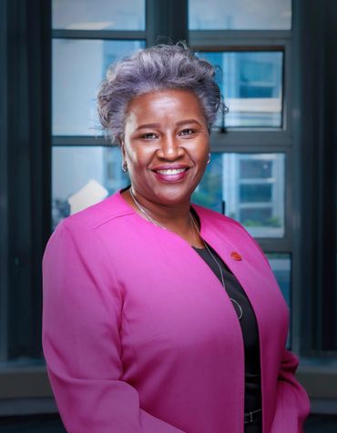 Confident woman in a bright pink blazer smiling indoors.