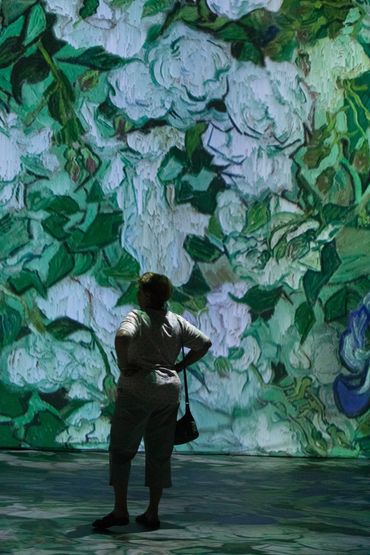 Person observing a large, vibrant floral artwork projection.