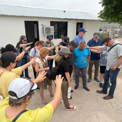 Group praying together outdoors near a white building.