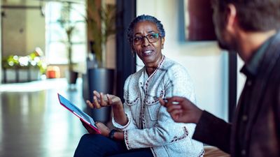 A woman holding document as she speaks to a man sitting next to her.