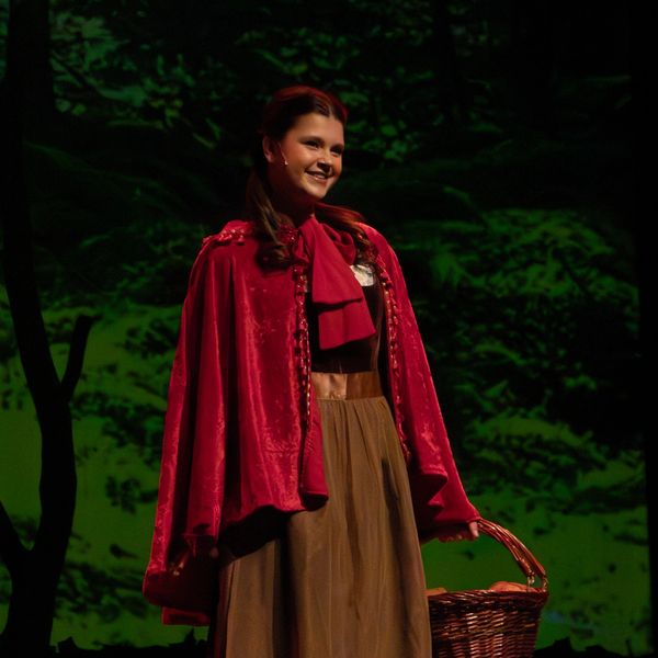 A girl wearing a red cape and holding a basket on stage.