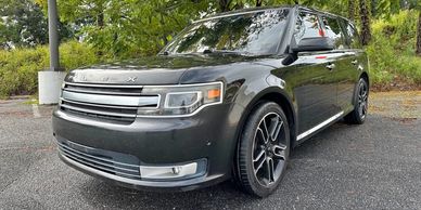 Black Ford Flex SUV parked outdoors near green trees.