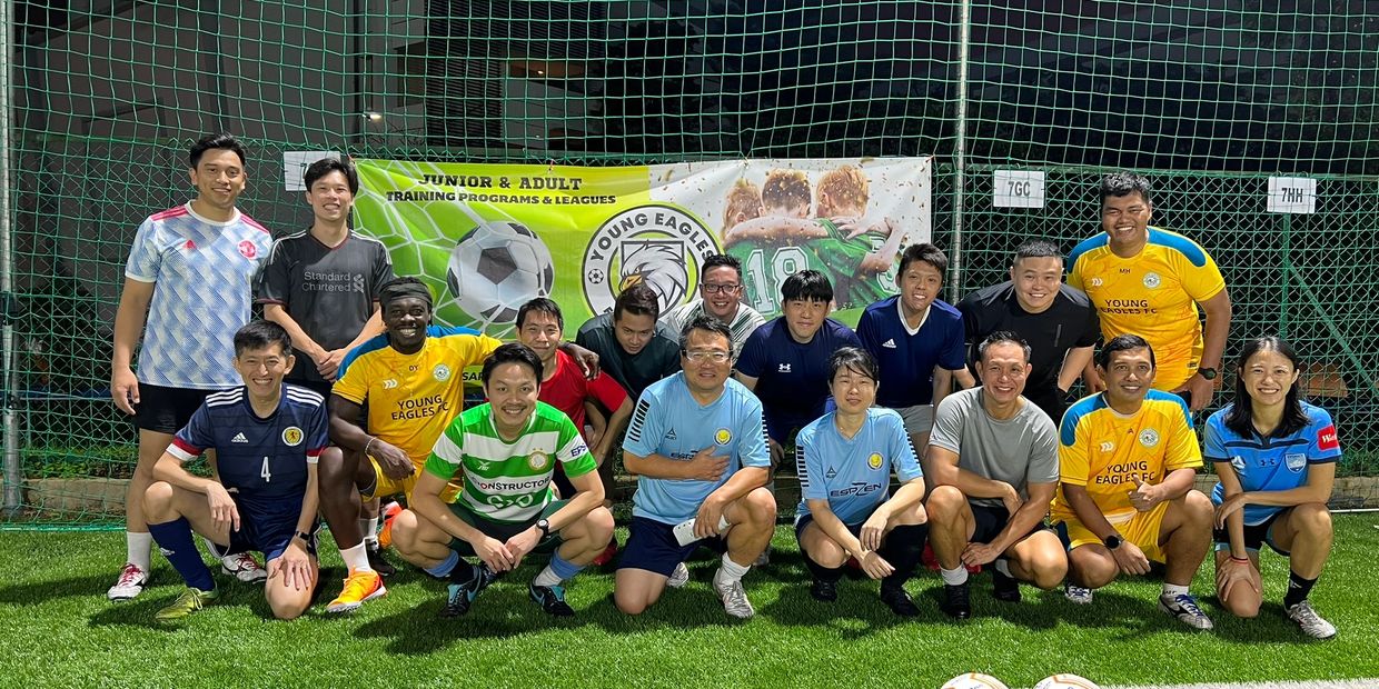Young Eagles FC adult players posing in front of the Young Eagles FC banner before a session.