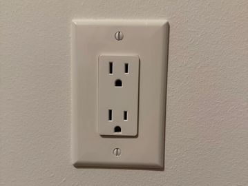 A white electrical outlet on a beige wall with a surprised face appearance.