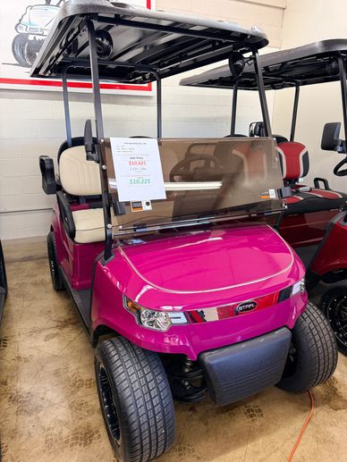 Bright pink golf cart with beige seats displayed indoors.