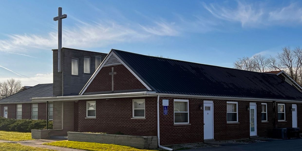 A brick church building with a tall cross against a blue sky.