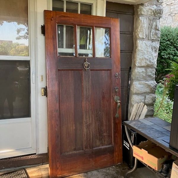 A vintage wooden door with glass panels leaning against a wall.