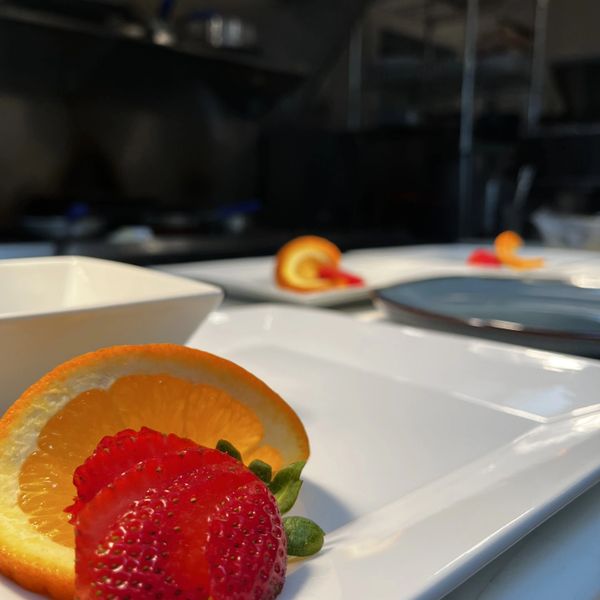 Close-up of sliced strawberries and orange on a white plate in a kitchen.