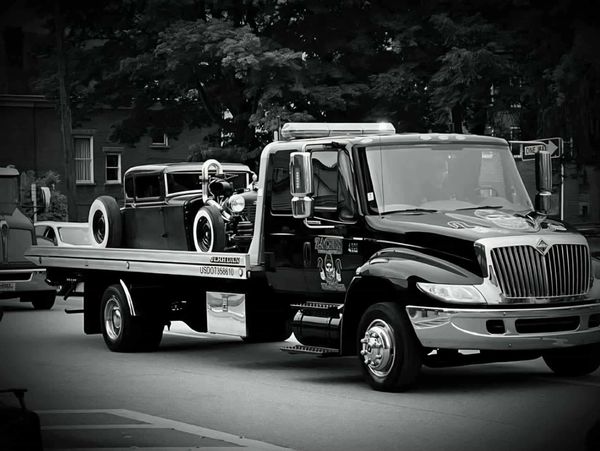 A modern tow truck carrying a vintage car on a city street.