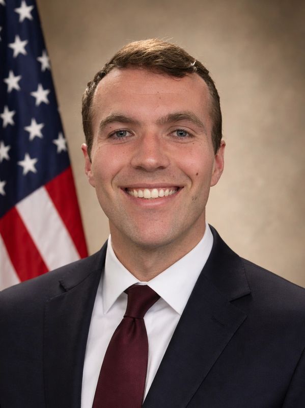 Young man in suit and tie smiling in front of the American flag.