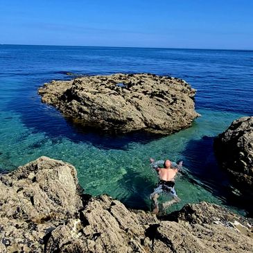 Person swimming in clear blue ocean near rocky shore.