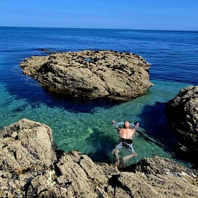 A person swimming in clear rocky coastal waters.