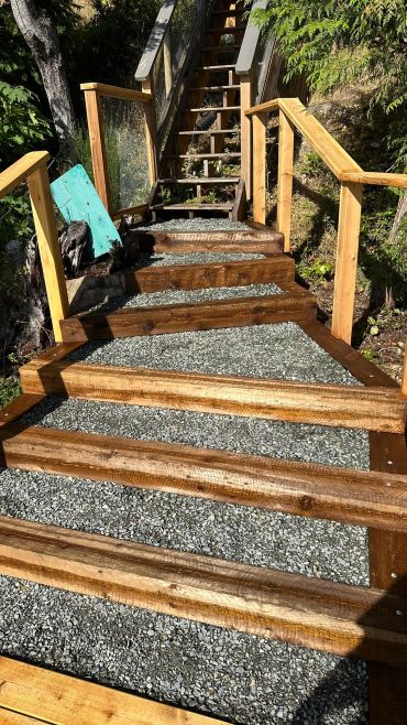 Wooden stairs with gravel steps and railings in a forested area.