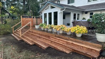 A wooden deck with steps and potted plants outside a white house.