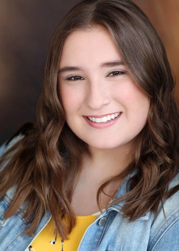 Smiling young woman with wavy brown hair and a denim jacket.
