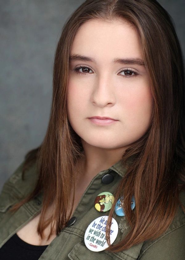 Young woman with long hair wearing a green jacket adorned with inspirational buttons.