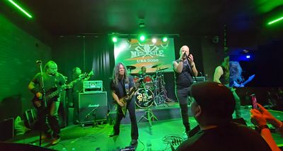 Rock band performing on stage with green lighting.