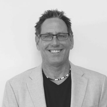 Smiling man in glasses and blazer against white background.