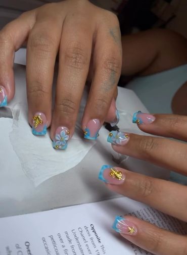 Blue French tip nails with gold and white flower decorations.