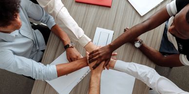 Photo by Eugene Angoluk (Pexels) of business people putting their hands together in a group huddle.
