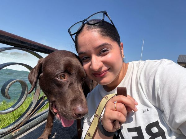 Woman smiling with her chocolate Labrador dog outdoors.