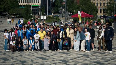 Large group posing outdoors in urban park on sunny day.