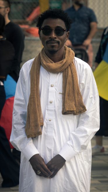 Man in white traditional attire with a brown scarf and sunglasses.