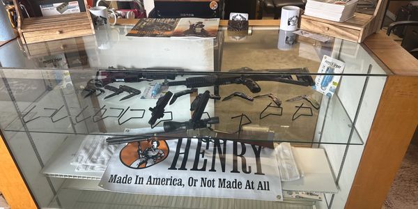 Gun store display case with firearms, knives, and promotional materials.