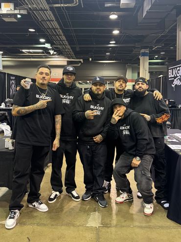 Group of six men posing indoors wearing matching black outfits.