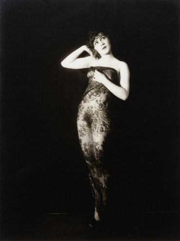 Vintage black-and-white photo of a woman in a lace dress striking a graceful pose.