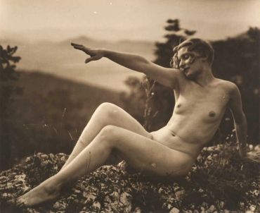 A vintage black and white photo of a nude woman posing outdoors on rocks.