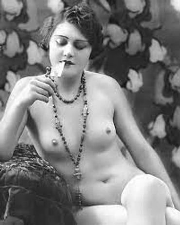 Vintage black-and-white photo of a woman posing nude with a long necklace.