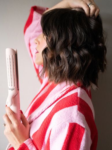 Woman with wavy hair holding a pink hair styling tool.