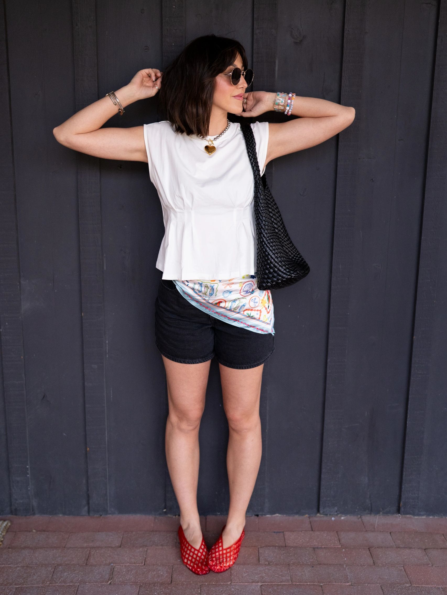 Woman posing stylishly in casual summer outfit with sunglasses and red shoes.