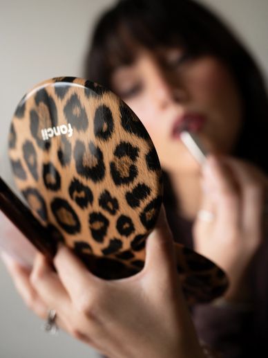 Woman applying lipstick using a leopard-print mirror.
