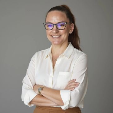 Smiling woman with glasses and folded arms.