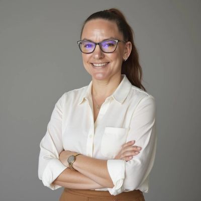 Smiling woman with glasses and ponytail, arms crossed.