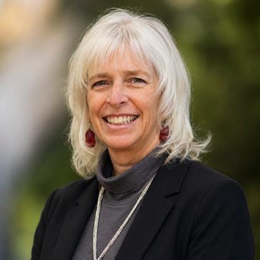 Smiling woman with white hair and black blazer.
