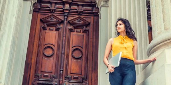 Woman standing by an ornate wooden door holding a notebook.