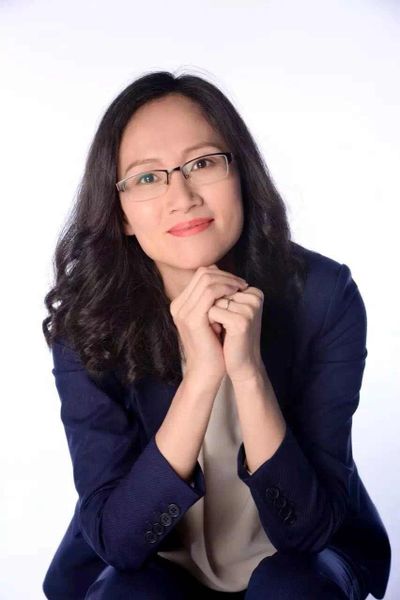 Confident woman with glasses wearing a navy blazer and smiling gently.