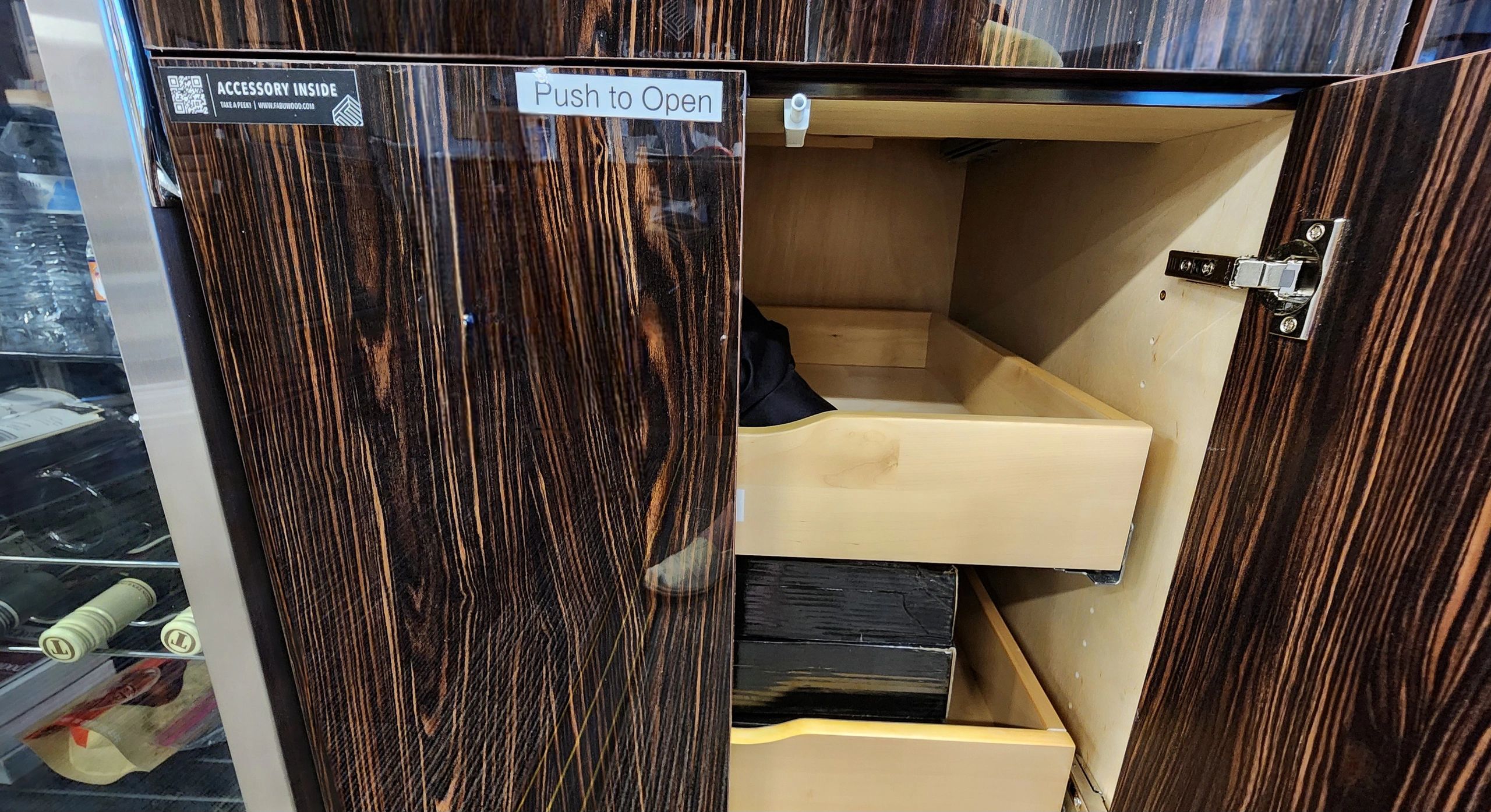 Open wooden cabinet with drawers and a glass door refrigerator beside it.