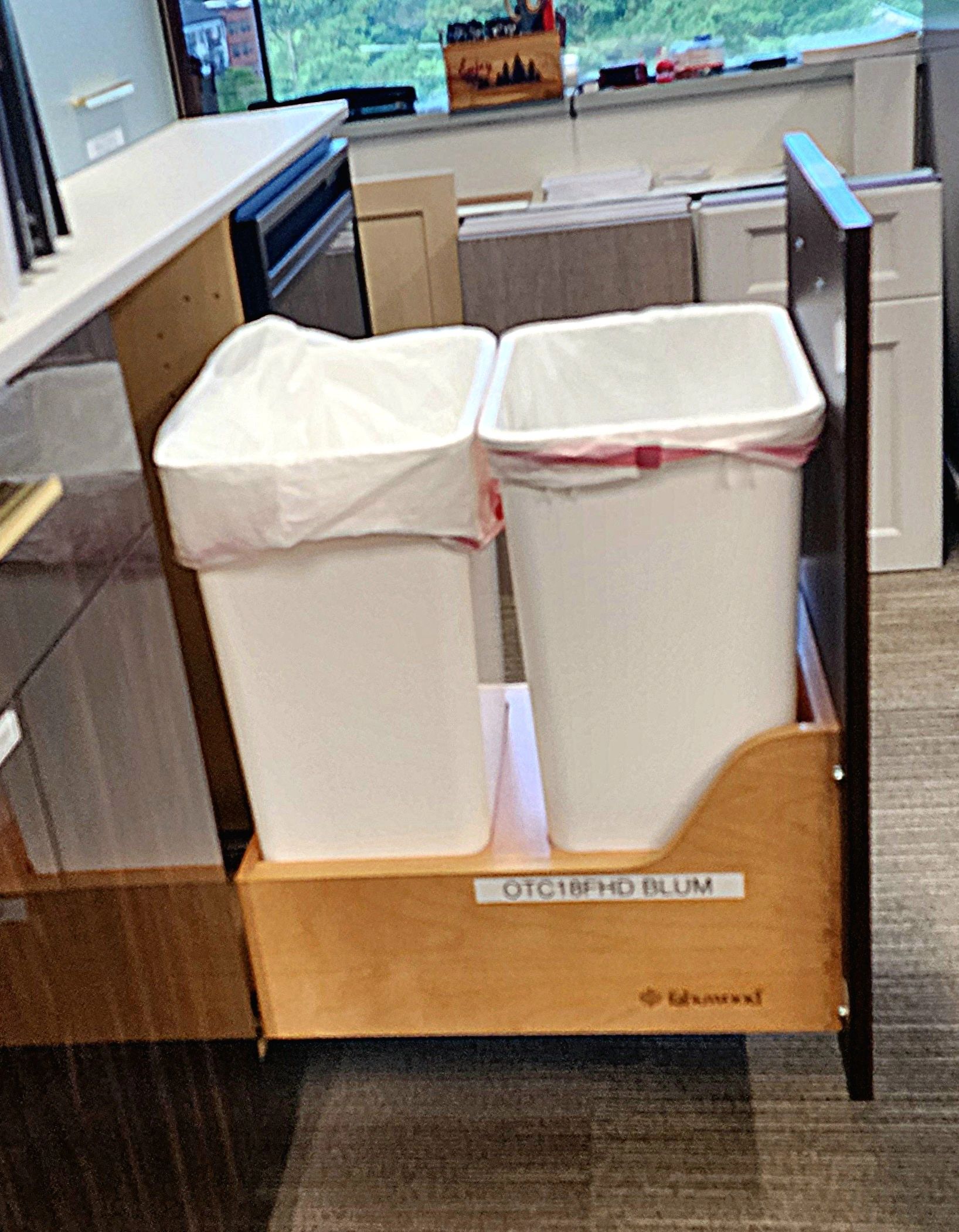 Two white trash bins with liners in a wooden pull-out cabinet.