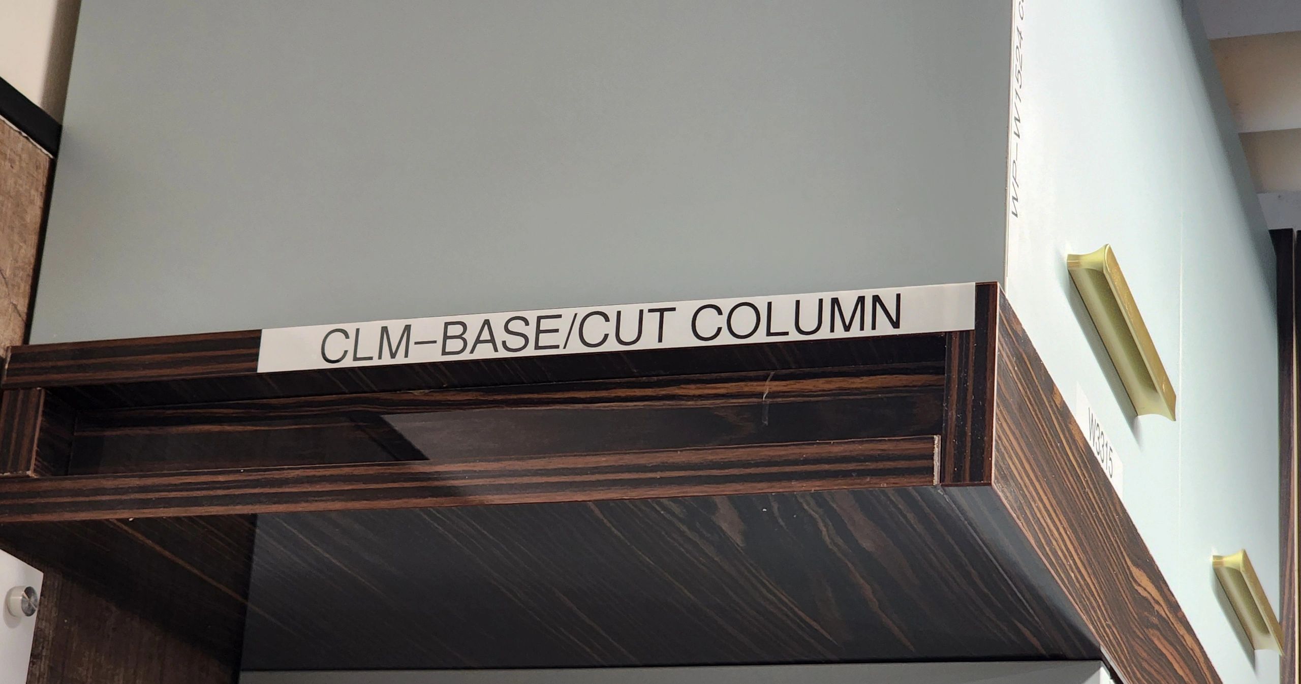 Sign reading 'CLM-BASE/CUT COLUMN' on a dark wood surface.