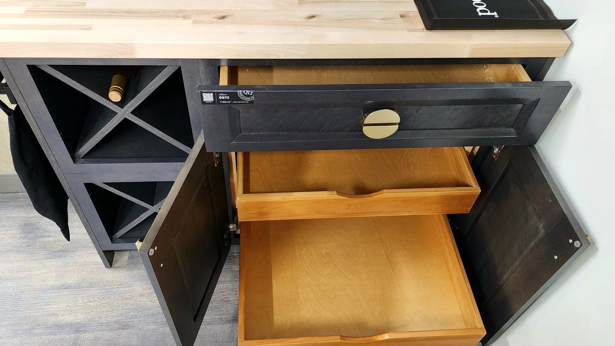 Open black kitchen cabinet with wooden drawers and a wine bottle.